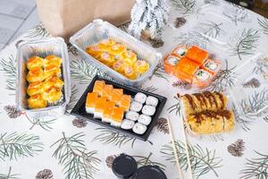 Delivery of sushi and rolls set top view on the table with a Christmas decor with a Christmas tree and a tablecloth with snowflakes, home cooking photo
