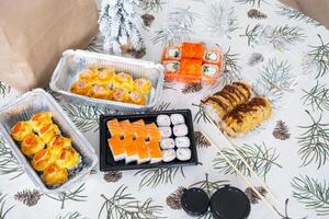 Delivery of sushi and rolls set top view on the table with a Christmas decor with a Christmas tree and a tablecloth with snowflakes, home cooking photo