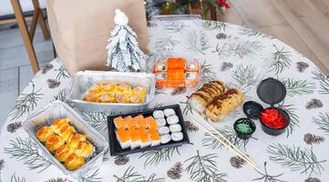 Delivery of sushi and rolls set top view on the table with a Christmas decor with a Christmas tree and a tablecloth with snowflakes, home cooking photo