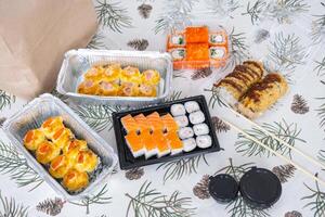 Delivery of sushi and rolls set top view on the table with a Christmas decor with a Christmas tree and a tablecloth with snowflakes, home cooking photo