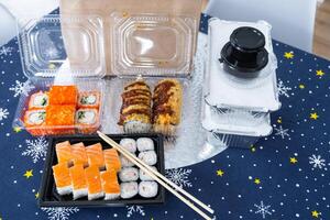 Delivery of sushi and rolls set top view on the table with a Christmas decor with a Christmas tree and a tablecloth with snowflakes, home cooking photo