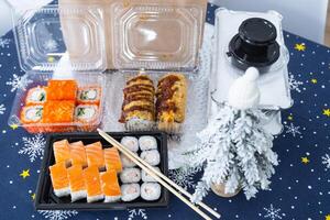 Delivery of sushi and rolls set top view on the table with a Christmas decor with a Christmas tree and a tablecloth with snowflakes, home cooking photo