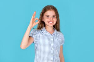 Portrait of optimistic friendly small girl show okay symbol isolated on blue color background photo