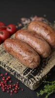 Chicken or pork sausages with salt, spices and herbs baked on the grill on a dark concrete background video