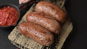 Chicken or pork sausages with salt, spices and herbs baked on the grill on a dark concrete background video