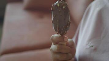 A Chocolate Ice Cream Bar Being Held in Hand While Sitting on a Comfortable Sofa video