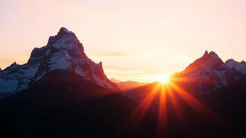 Towering mountains with snowy peaks bathed in the warm light of sunrise, casting long shadows and illuminating the sky with hues of pink, orange, and gold. photo