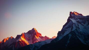 Towering mountains with snowy peaks bathed in the warm light of sunrise, casting long shadows and illuminating the sky with hues of pink, orange, and gold. photo