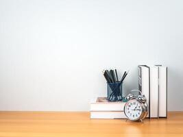 Back to school concept, Pencil on book stack and alarm clock on wooden table workspace area and white wall, Concept of time to study, read books, Concept of preparing for exams. photo