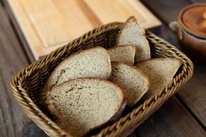 Basket filled with slices of bread. The basket is woven and sits on a wooden table. There are also two ceramic pots with lids nearby, adding a rustic feel to the scene. photo