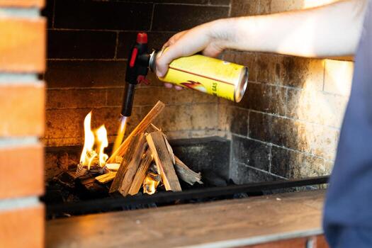 This image shows a fireplace being lit using a butane torch. The flame from the torch is helping ignite pieces of wood arranged in the fireplace. photo