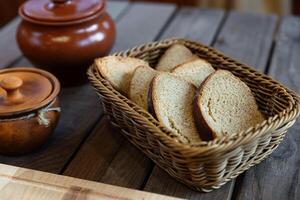 Basket filled with slices of bread. The basket is woven and sits on a wooden table. There are also two ceramic pots with lids nearby, adding a rustic feel to the scene. photo