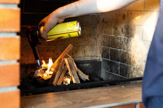 This image shows a fireplace being lit using a butane torch. The flame from the torch is helping ignite pieces of wood arranged in the fireplace. photo