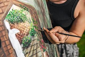 Close-up of someone skillfully painting on a canvas. The artwork looks like it depicts a rustic scene, possibly featuring elements like bricks or wood, giving it a cozy, homely feel. photo