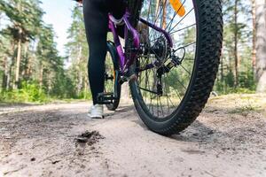 Close-up of a bicycle parked on a dirt trail, with a focus on the kickstand. The bike's rugged tires are well-suited for trail riding, and the scene suggests a forest environment. photo