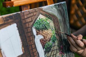 Close-up of someone skillfully painting on a canvas. The artwork looks like it depicts a rustic scene, possibly featuring elements like bricks or wood, giving it a cozy, homely feel. photo