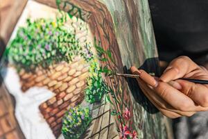 Close-up of someone skillfully painting on a canvas. The artwork looks like it depicts a rustic scene, possibly featuring elements like bricks or wood, giving it a cozy, homely feel. photo