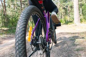 Close-up of a bicycle parked on a dirt trail, with a focus on the kickstand. The bike's rugged tires are well-suited for trail riding, and the scene suggests a forest environment. photo