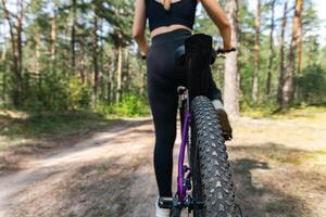 Close-up of a bicycle parked on a dirt trail, with a focus on the kickstand. The bike's rugged tires are well-suited for trail riding, and the scene suggests a forest environment. photo