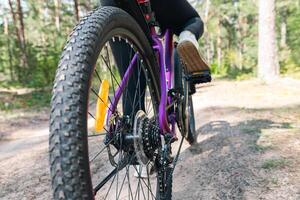 Close-up of a bicycle parked on a dirt trail, with a focus on the kickstand. The bike's rugged tires are well-suited for trail riding, and the scene suggests a forest environment. photo