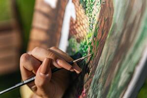 Close-up of someone skillfully painting on a canvas. The artwork looks like it depicts a rustic scene, possibly featuring elements like bricks or wood, giving it a cozy, homely feel. photo