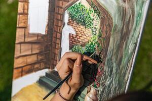 Close-up of someone skillfully painting on a canvas. The artwork looks like it depicts a rustic scene, possibly featuring elements like bricks or wood, giving it a cozy, homely feel. photo