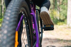 Close-up of a bicycle parked on a dirt trail, with a focus on the kickstand. The bike's rugged tires are well-suited for trail riding, and the scene suggests a forest environment. photo