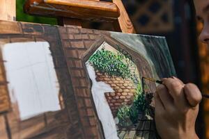 Close-up of someone skillfully painting on a canvas. The artwork looks like it depicts a rustic scene, possibly featuring elements like bricks or wood, giving it a cozy, homely feel. photo