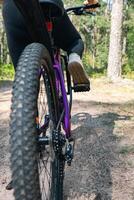 Close-up of a bicycle parked on a dirt trail, with a focus on the kickstand. The bike's rugged tires are well-suited for trail riding, and the scene suggests a forest environment. photo