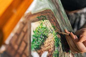 Close-up of someone skillfully painting on a canvas. The artwork looks like it depicts a rustic scene, possibly featuring elements like bricks or wood, giving it a cozy, homely feel. photo