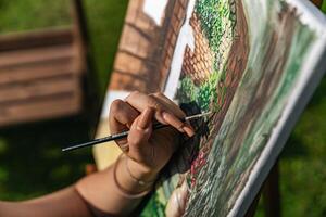 Close-up of someone skillfully painting on a canvas. The artwork looks like it depicts a rustic scene, possibly featuring elements like bricks or wood, giving it a cozy, homely feel. photo