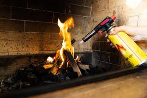 This image shows a fireplace being lit using a butane torch. The flame from the torch is helping ignite pieces of wood arranged in the fireplace. photo