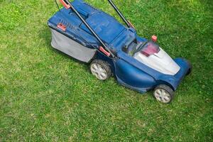 Mowing or cutting the very long grass with a green lawn mower in the summer sun photo