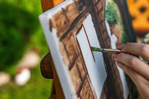 Close-up of someone skillfully painting on a canvas. The artwork looks like it depicts a rustic scene, possibly featuring elements like bricks or wood, giving it a cozy, homely feel. photo