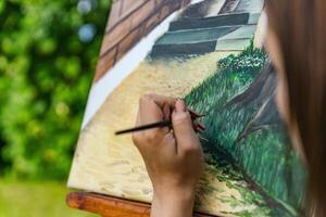 Close-up of someone skillfully painting on a canvas. The artwork looks like it depicts a rustic scene, possibly featuring elements like bricks or wood, giving it a cozy, homely feel. photo
