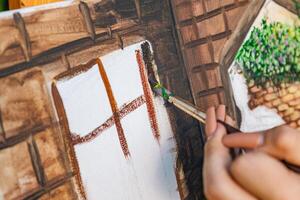Close-up of someone skillfully painting on a canvas. The artwork looks like it depicts a rustic scene, possibly featuring elements like bricks or wood, giving it a cozy, homely feel. photo