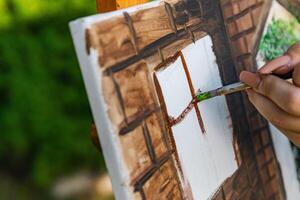 Close-up of someone skillfully painting on a canvas. The artwork looks like it depicts a rustic scene, possibly featuring elements like bricks or wood, giving it a cozy, homely feel. photo