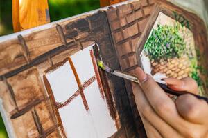Close-up of someone skillfully painting on a canvas. The artwork looks like it depicts a rustic scene, possibly featuring elements like bricks or wood, giving it a cozy, homely feel. photo