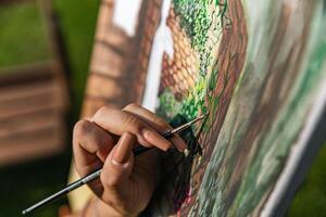 Close-up of someone skillfully painting on a canvas. The artwork looks like it depicts a rustic scene, possibly featuring elements like bricks or wood, giving it a cozy, homely feel. photo