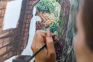 Close-up of someone skillfully painting on a canvas. The artwork looks like it depicts a rustic scene, possibly featuring elements like bricks or wood, giving it a cozy, homely feel. photo
