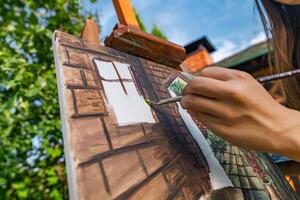 Close-up of someone skillfully painting on a canvas. The artwork looks like it depicts a rustic scene, possibly featuring elements like bricks or wood, giving it a cozy, homely feel. photo