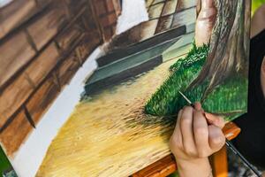 Close-up of someone skillfully painting on a canvas. The artwork looks like it depicts a rustic scene, possibly featuring elements like bricks or wood, giving it a cozy, homely feel. photo