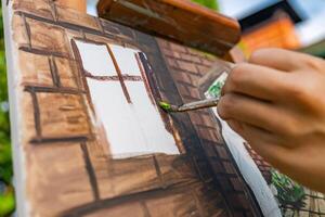 Close-up of someone skillfully painting on a canvas. The artwork looks like it depicts a rustic scene, possibly featuring elements like bricks or wood, giving it a cozy, homely feel. photo