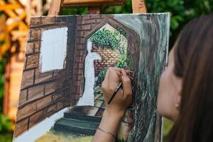 Close-up of someone skillfully painting on a canvas. The artwork looks like it depicts a rustic scene, possibly featuring elements like bricks or wood, giving it a cozy, homely feel. photo