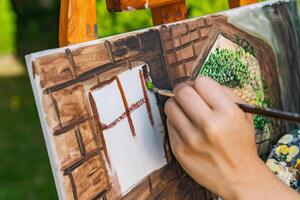 Close-up of someone skillfully painting on a canvas. The artwork looks like it depicts a rustic scene, possibly featuring elements like bricks or wood, giving it a cozy, homely feel. photo