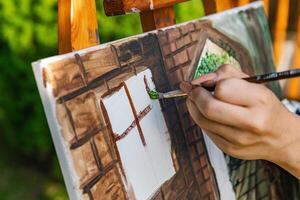 Close-up of someone skillfully painting on a canvas. The artwork looks like it depicts a rustic scene, possibly featuring elements like bricks or wood, giving it a cozy, homely feel. photo
