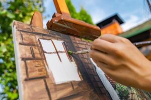 Close-up of someone skillfully painting on a canvas. The artwork looks like it depicts a rustic scene, possibly featuring elements like bricks or wood, giving it a cozy, homely feel. photo
