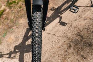 Close-up of a bicycle parked on a dirt trail, with a focus on the kickstand. The bike's rugged tires are well-suited for trail riding, and the scene suggests a forest environment. photo