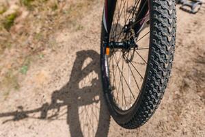 Close-up of a bicycle parked on a dirt trail, with a focus on the kickstand. The bike's rugged tires are well-suited for trail riding, and the scene suggests a forest environment. photo
