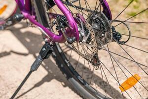 Close-up of a bicycle parked on a dirt trail, with a focus on the kickstand. The bike's rugged tires are well-suited for trail riding, and the scene suggests a forest environment. photo
